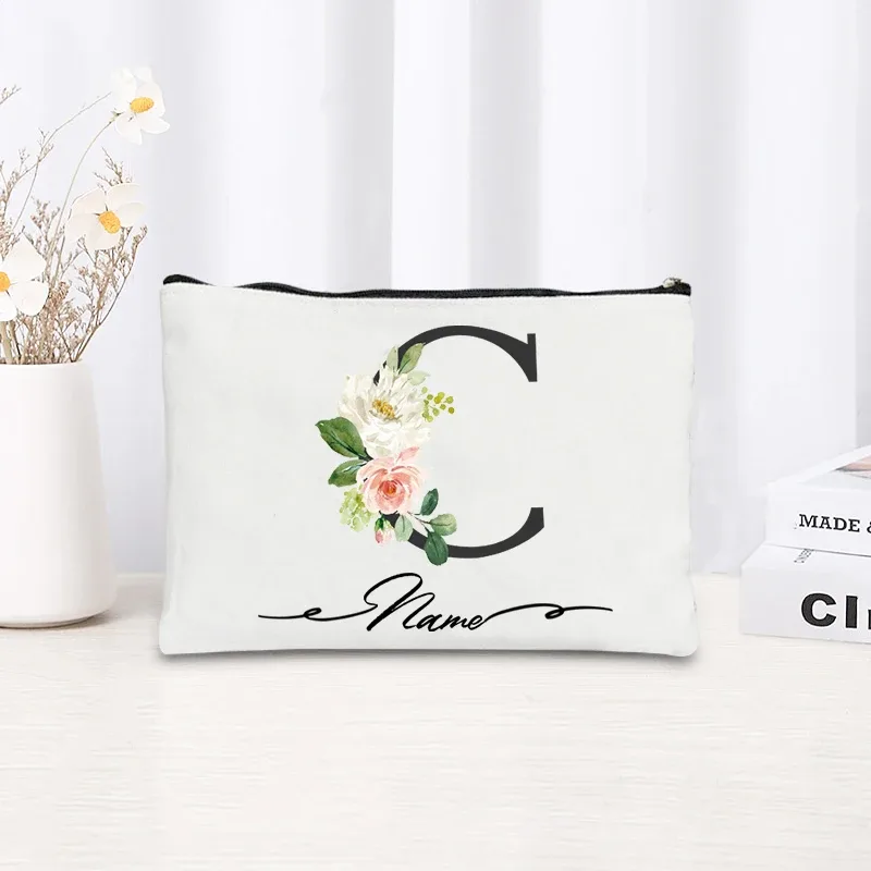 pochette personnalisée en toile noire à motif floral avec initiale en écriture cursive, trousse de toilette fine et compacte pour femmes, idéale pour les voyages et l'usage quotidien.