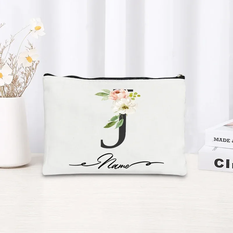 pochette personnalisée en toile noire à motif floral avec initiale en écriture cursive, trousse de toilette fine et compacte pour femmes, idéale pour les voyages et l'usage quotidien.