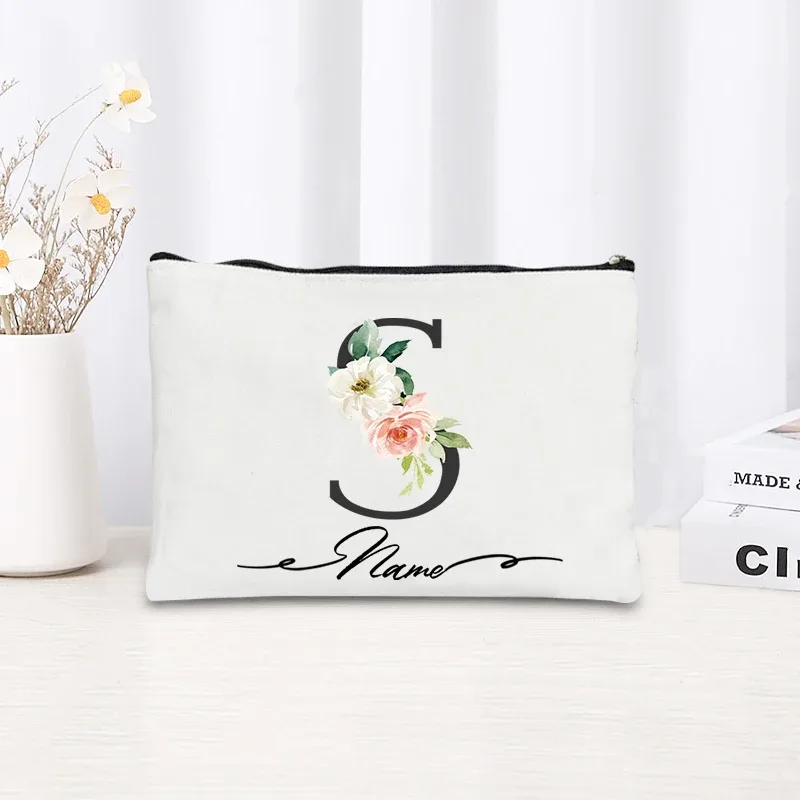 pochette personnalisée en toile noire à motif floral avec initiale en écriture cursive, trousse de toilette fine et compacte pour femmes, idéale pour les voyages et l'usage quotidien.