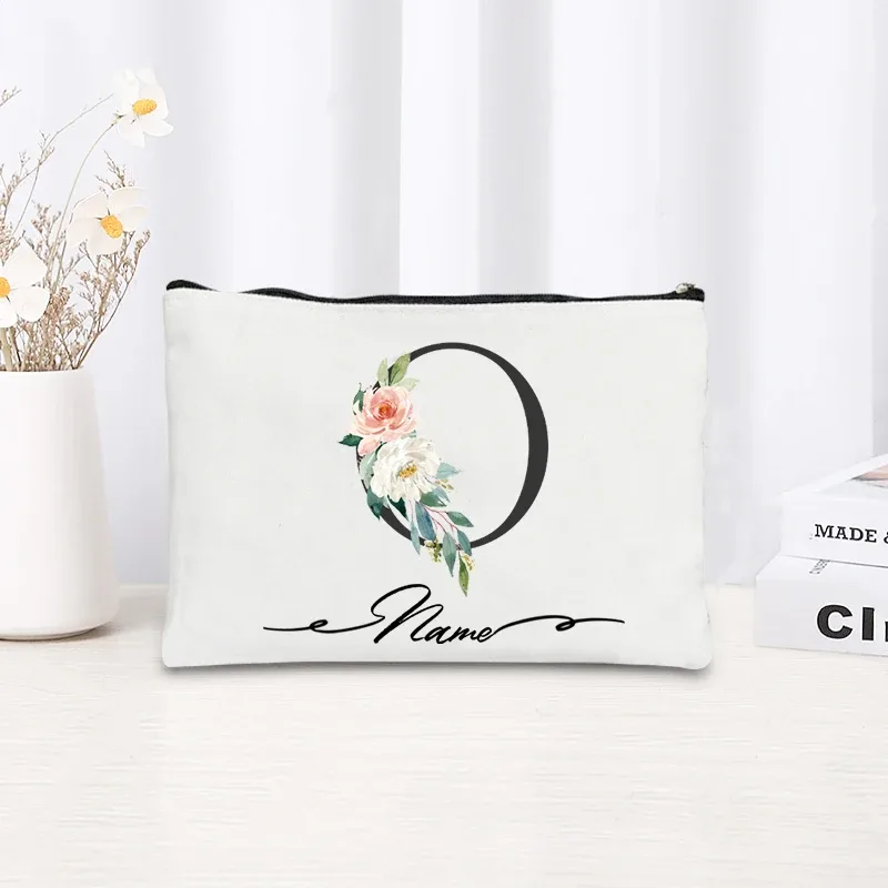 pochette personnalisée en toile noire à motif floral avec initiale en écriture cursive, trousse de toilette fine et compacte pour femmes, idéale pour les voyages et l'usage quotidien.