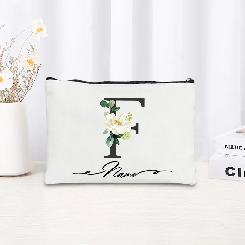 pochette personnalisée en toile noire à motif floral avec initiale en écriture cursive, trousse de toilette fine et compacte pour femmes, idéale pour les voyages et l'usage quotidien.