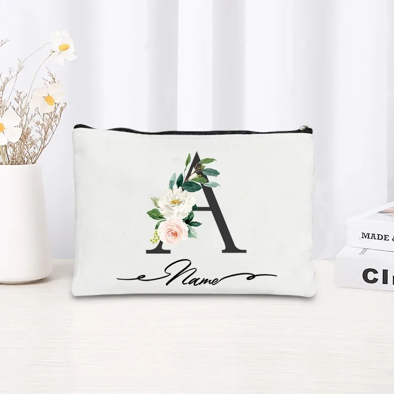pochette personnalisée en toile noire à motif floral avec initiale en écriture cursive, trousse de toilette fine et compacte pour femmes, idéale pour les voyages et l'usage quotidien.