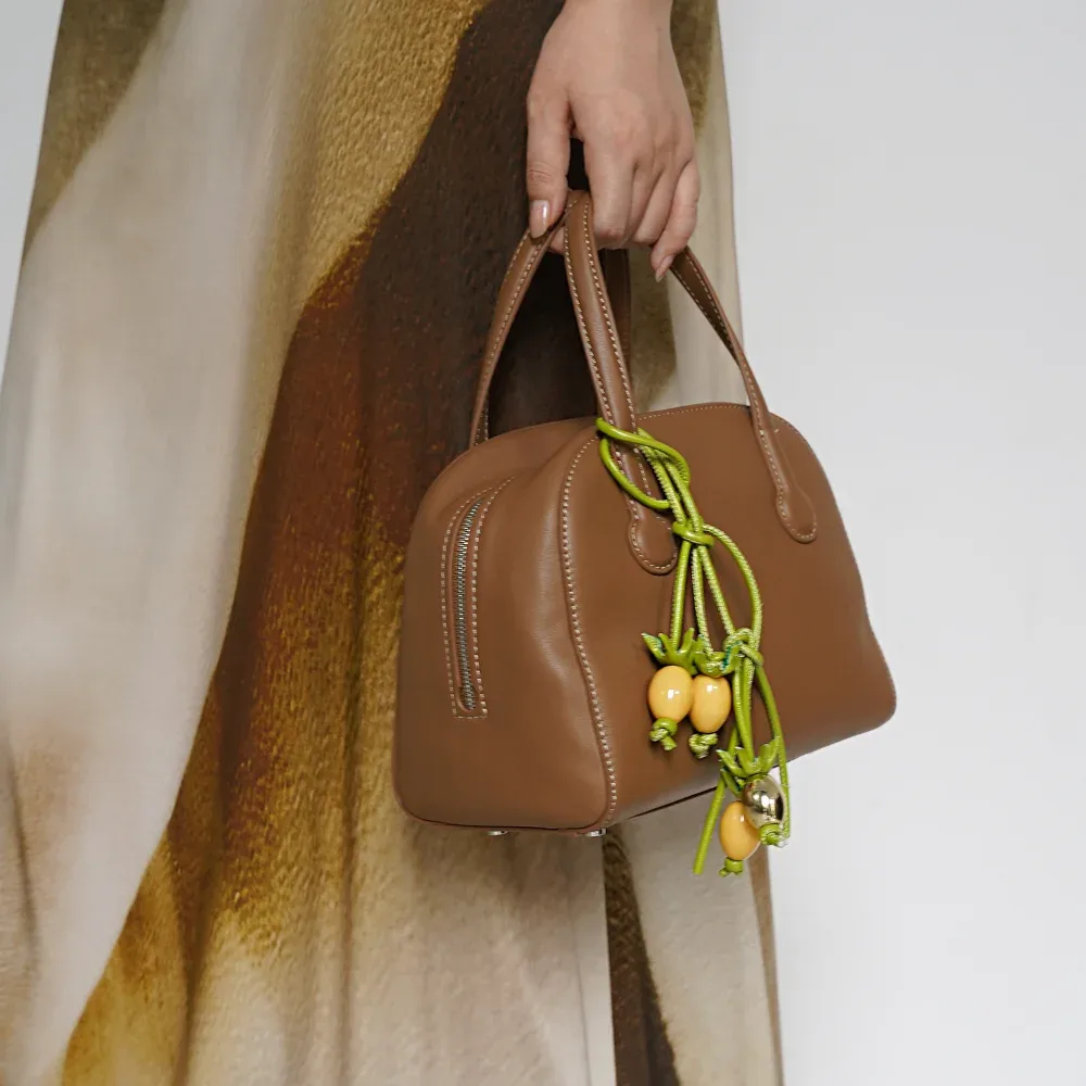 sacoche oval cuir marron clous dorés poignées courtes chaîne vert pompons rouges jaunes accessoire voyage léger