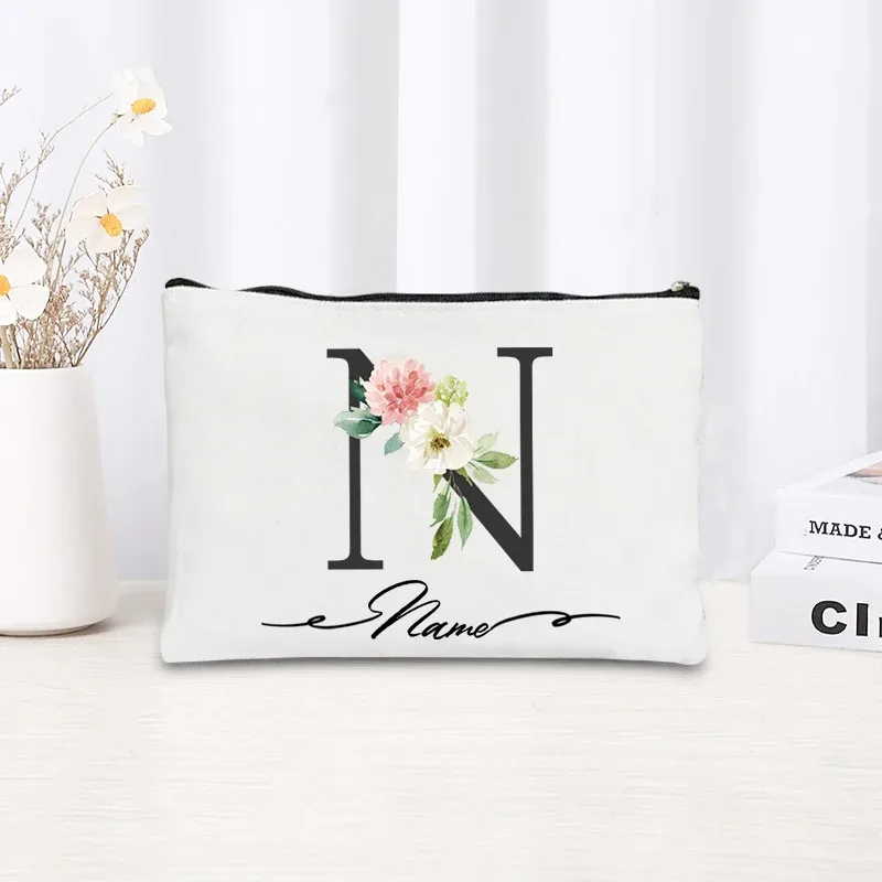 pochette personnalisée en toile noire à motif floral avec initiale en écriture cursive, trousse de toilette fine et compacte pour femmes, idéale pour les voyages et l'usage quotidien.