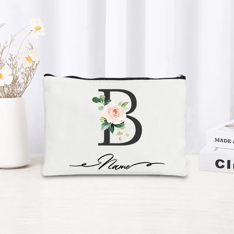 pochette personnalisée en toile noire à motif floral avec initiale en écriture cursive, trousse de toilette fine et compacte pour femmes, idéale pour les voyages et l'usage quotidien.