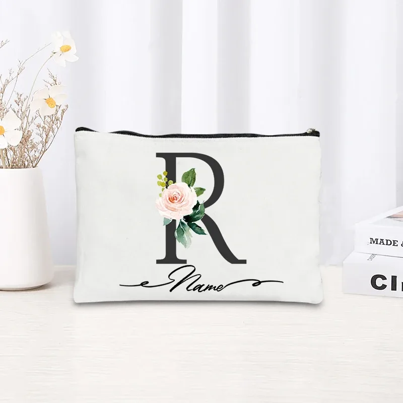 pochette personnalisée en toile noire à motif floral avec initiale en écriture cursive, trousse de toilette fine et compacte pour femmes, idéale pour les voyages et l'usage quotidien.