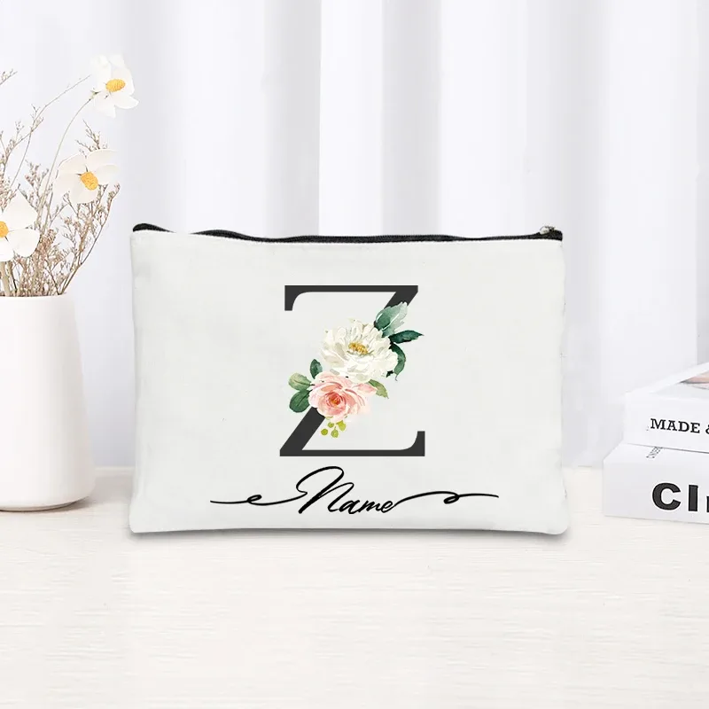 pochette personnalisée en toile noire à motif floral avec initiale en écriture cursive, trousse de toilette fine et compacte pour femmes, idéale pour les voyages et l'usage quotidien.