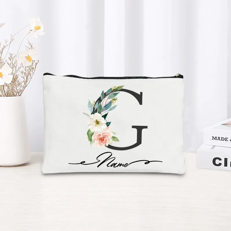 pochette personnalisée en toile noire à motif floral avec initiale en écriture cursive, trousse de toilette fine et compacte pour femmes, idéale pour les voyages et l'usage quotidien.