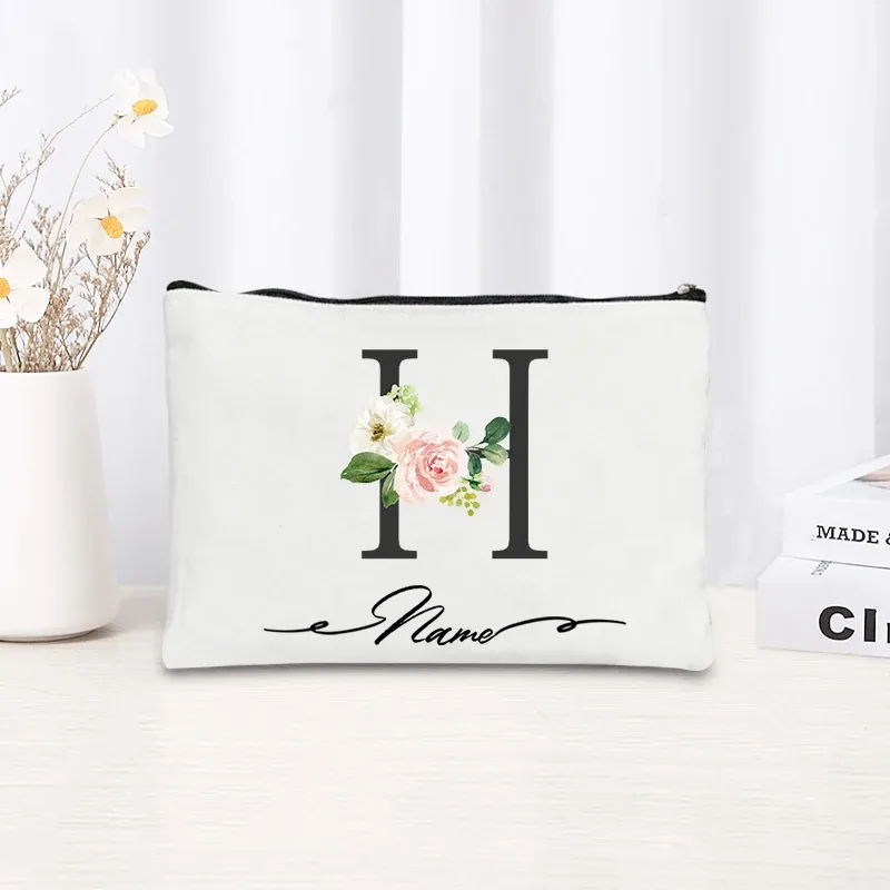 pochette personnalisée en toile noire à motif floral avec initiale en écriture cursive, trousse de toilette fine et compacte pour femmes, idéale pour les voyages et l'usage quotidien.