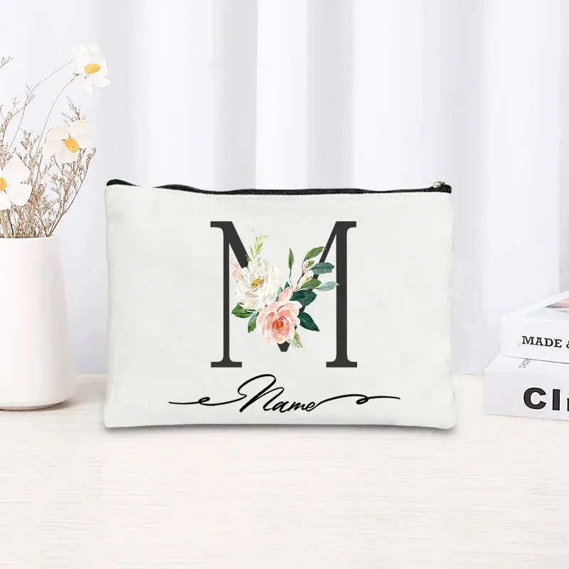 pochette personnalisée en toile noire à motif floral avec initiale en écriture cursive, trousse de toilette fine et compacte pour femmes, idéale pour les voyages et l'usage quotidien.
