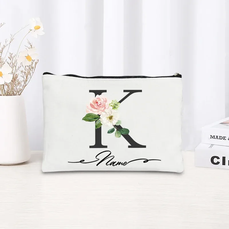 pochette personnalisée en toile noire à motif floral avec initiale en écriture cursive, trousse de toilette fine et compacte pour femmes, idéale pour les voyages et l'usage quotidien.