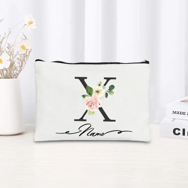 pochette personnalisée en toile noire à motif floral avec initiale en écriture cursive, trousse de toilette fine et compacte pour femmes, idéale pour les voyages et l'usage quotidien.