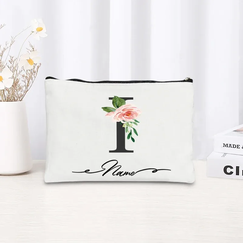 pochette personnalisée en toile noire à motif floral avec initiale en écriture cursive, trousse de toilette fine et compacte pour femmes, idéale pour les voyages et l'usage quotidien.
